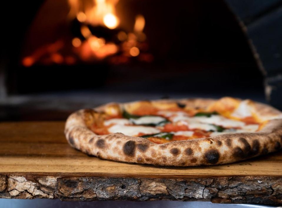 Wood fired pizza with melted mozzarella and basil, fresh out of a wood burning oven