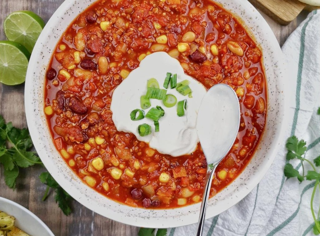 A bowl of vegetable bean chili soup topped with sour cream and green onion